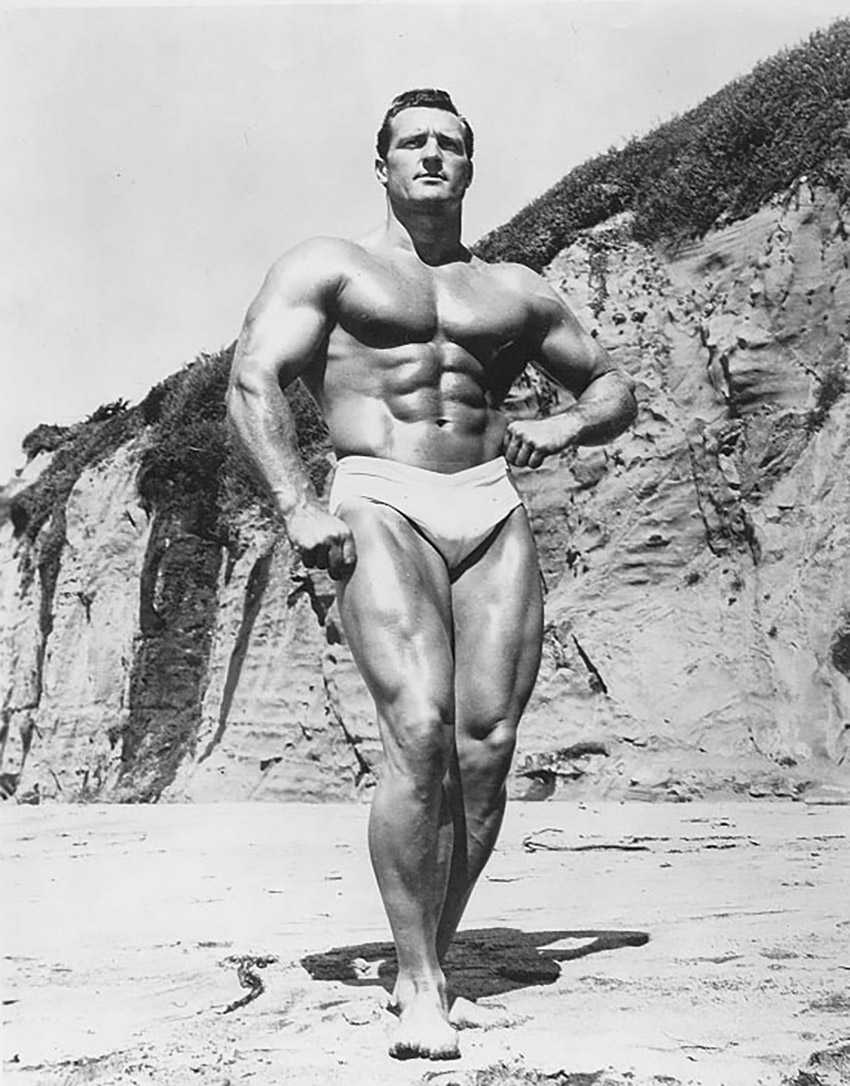 Clarence Ross on the beach posing in swimming shorts