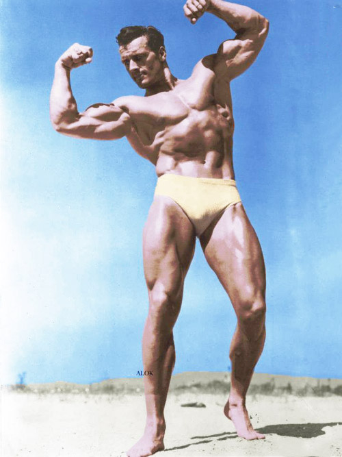 Clarence Ross photograph in colour in swimming shorts on beach flexing both biceps 