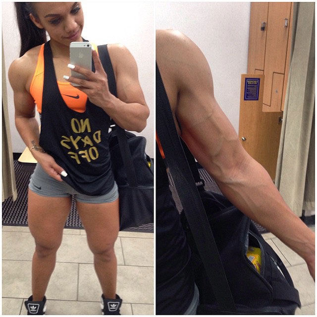 Nadia Amy flexing her right bicep and standing in short shorts also flexing her large quads 