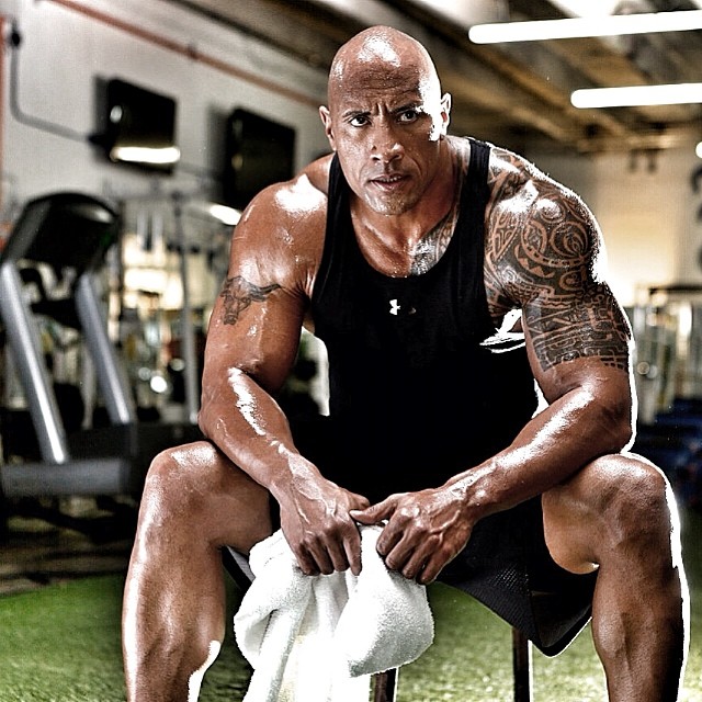 Dwayne Johnson The Rock sitting exhausted in the gym, looking muscular