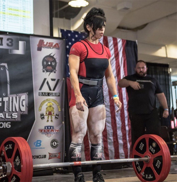 Marisa Inda Standing in front of the barbell in a power lifting competition ready to take the weight 