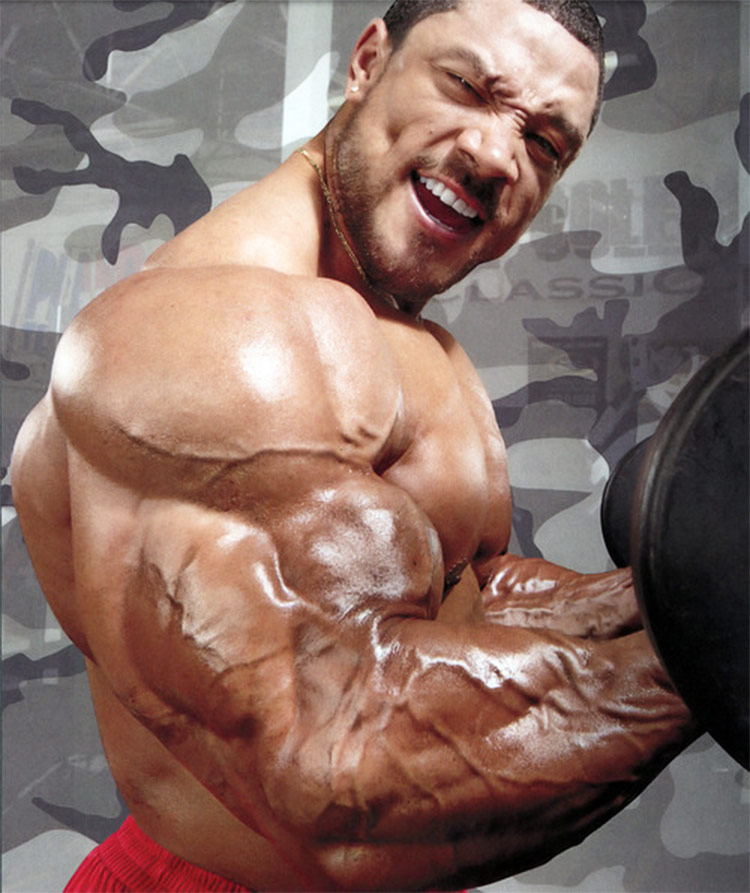 Roelly WInklaar flexing his arms, showing the muscular definition on his biceps and triceps.