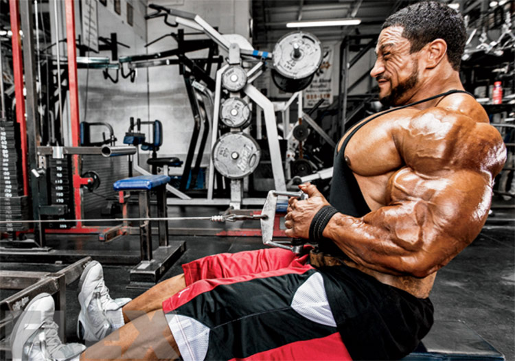 Roelly Winklaar training in the gym, pulling a weight and tensing his muscles. 