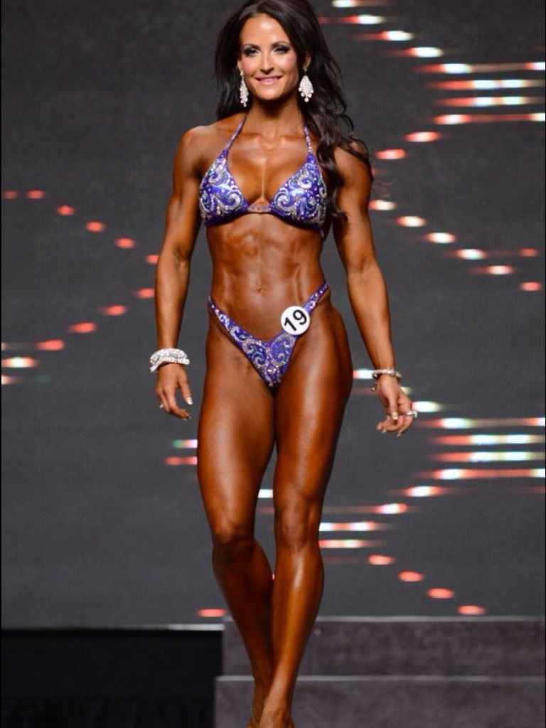 Erin Stern walking towards judges on the stage, proudly presenting her physique and smiling