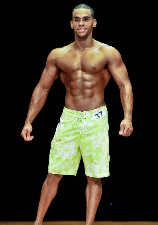 Alex Los Angeles on stage competing in men's figure competition wearing long green shorts