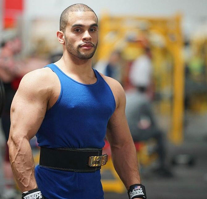 Alex Los Angeles wearing a lifting belt in the gym looking big and bulky while wearing a blue vest