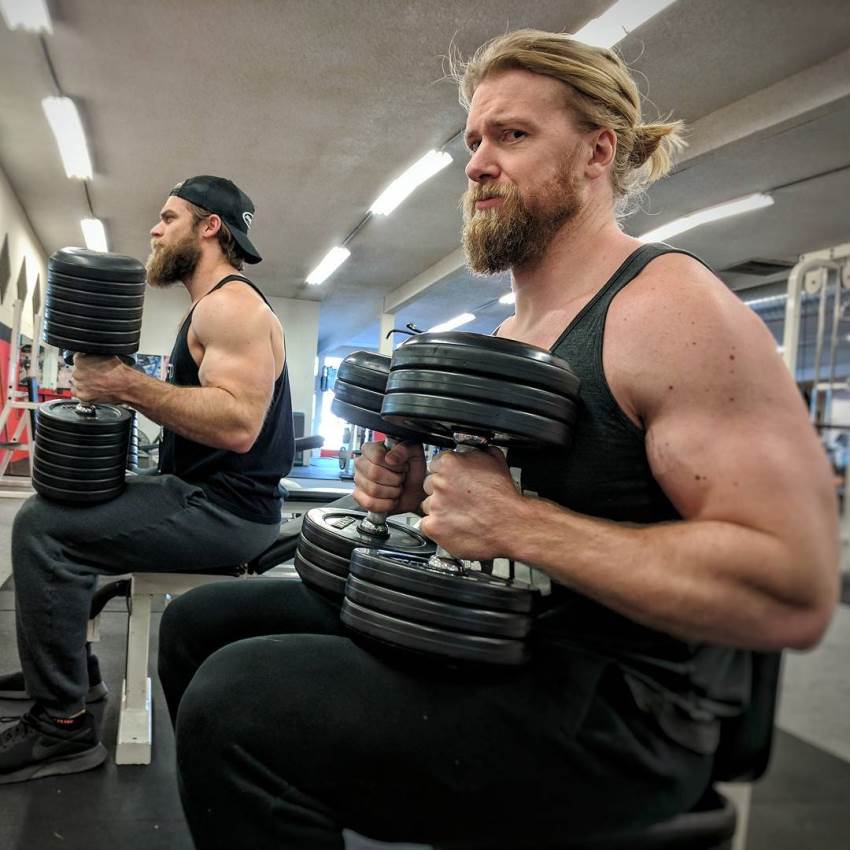 Buff Dudes preparing to do a set in the gym, sitting on a bench next to each other