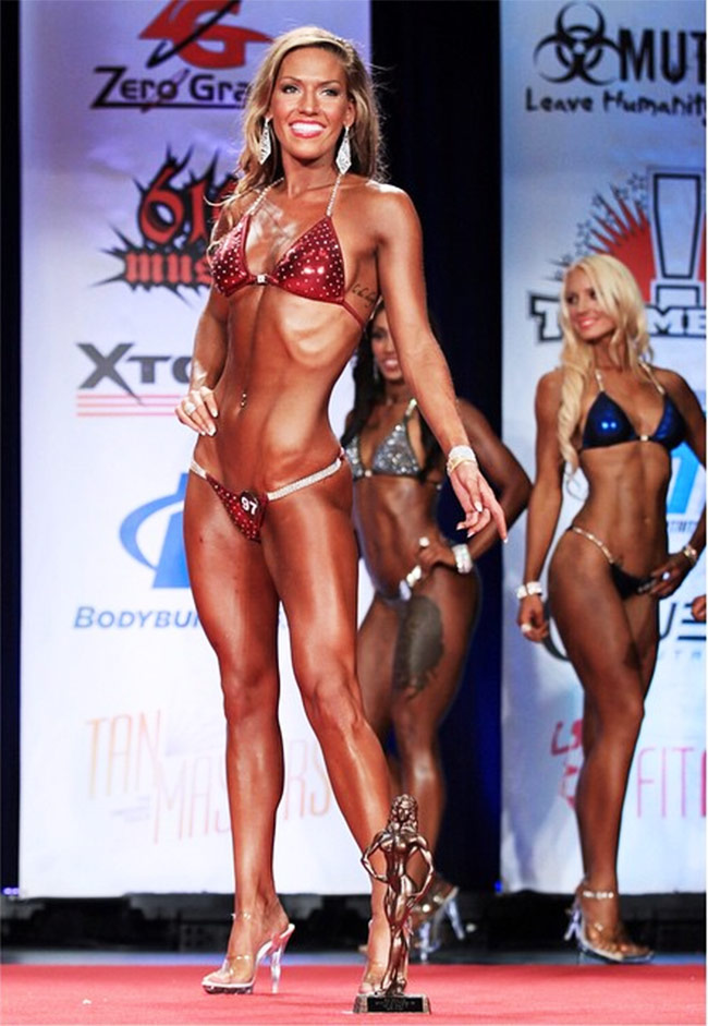 Courtney Gardner posing on stage with her trophy after winning the 2015 NPC Spartan championships as a bikini athlete.
