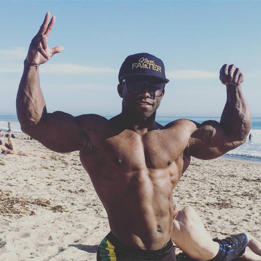 Damion Ricketts standing on the beach and tensing his biceps