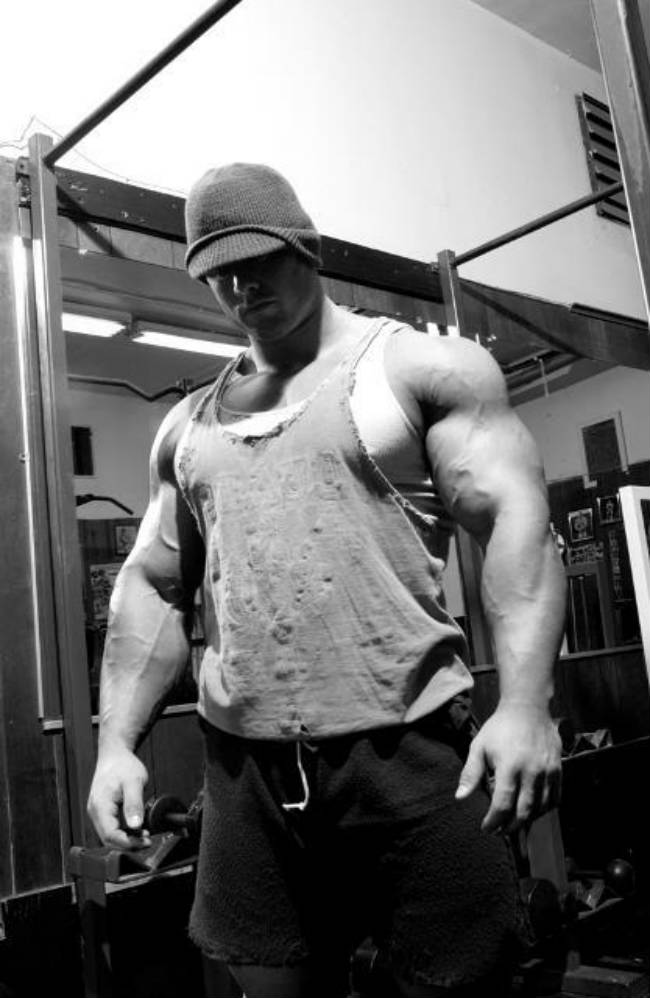 Frank Mcgrath stands in a darkened gym room wearing a ripped vest