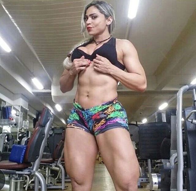 Gleycelilia Bracca flexing her abs in the gym while wearing short shorts and a tight black top 