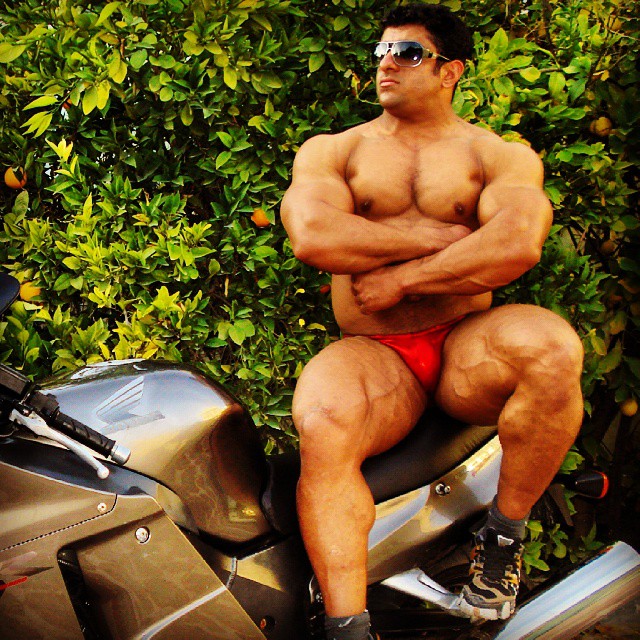 Hadi Choopan sitting on a motorbike with his arms crossed, as he shows his big and muscular physique