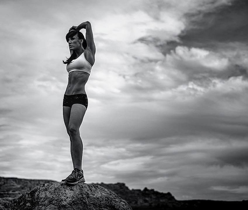 Heidi Carlsen stretching her arms and lats outdoors, standing on a rock