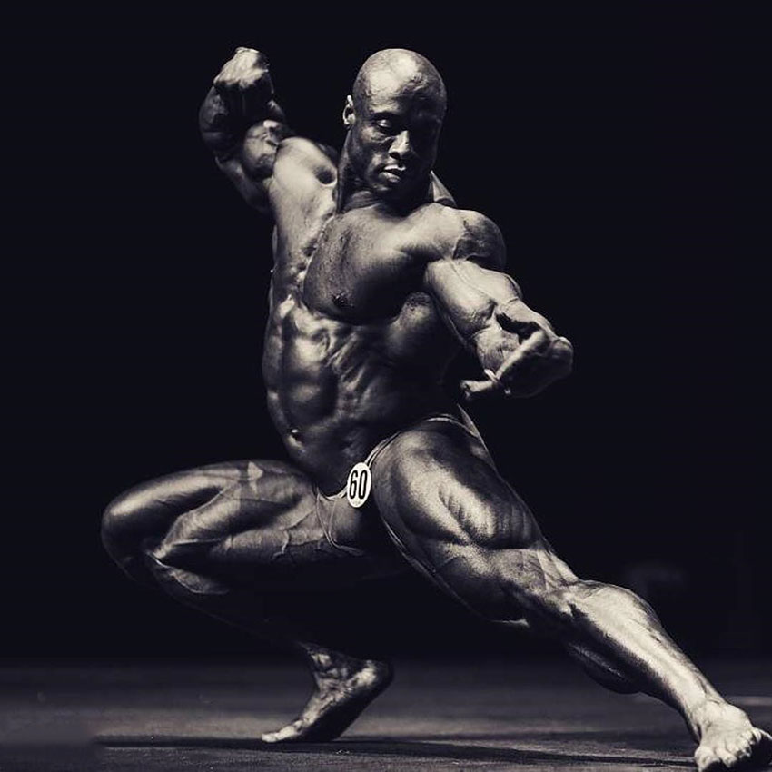 Jeff Beckham posing on a bodybuilding stage crouched down in an artistic fashion 