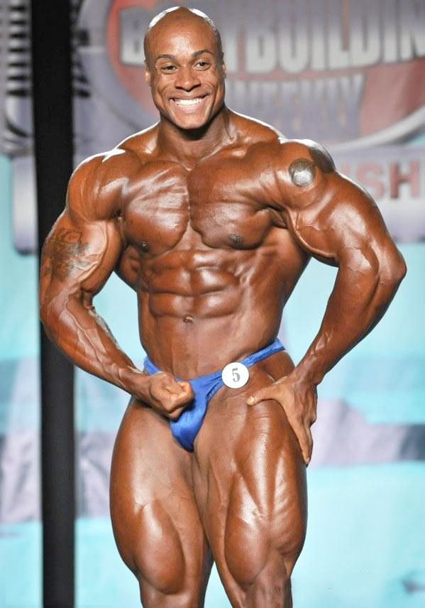 Jeff Beckham smiling and posing on a bodybuilding stage looking muscular and ripped in blue trunks 