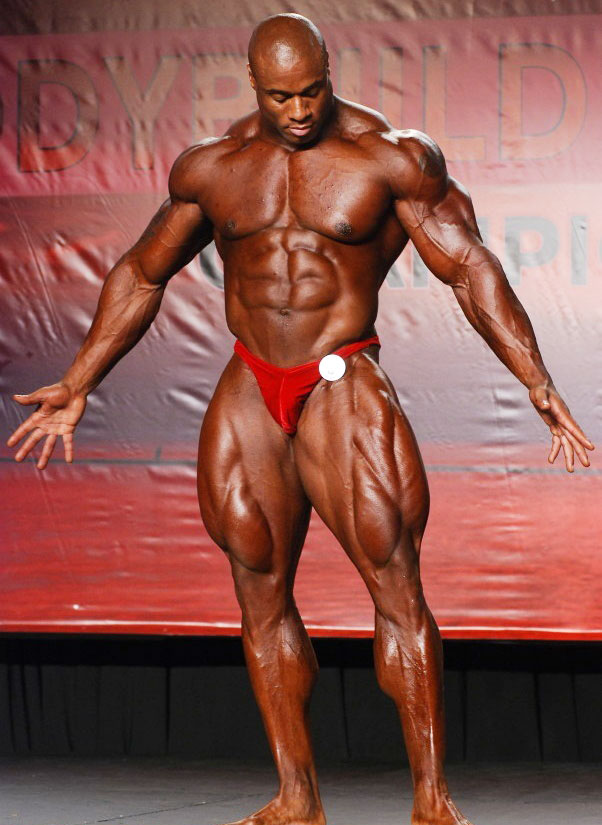 Jeff Beckham posing on a bodybuilding stage in red trunks looking huge and strong 