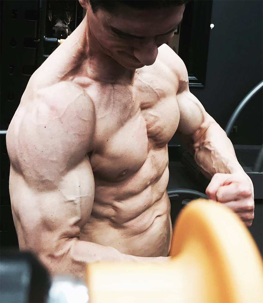 Jeff Cavaliere showing how shredded he is by tensing his arms, abs and chest while posing for a photo.