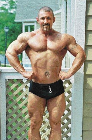 Jerry Ward in black shorts, in a front lat spred pose, showing his ripped body