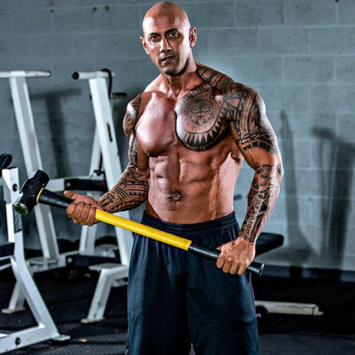 Jerry Ward with a hammer in his hand, looking directly into the camera, while showing his muscular physique