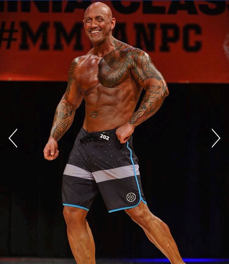 Jerry Ward posing his his dark blue trunks on the stage, while smiling and showing his ripped physique to the audience