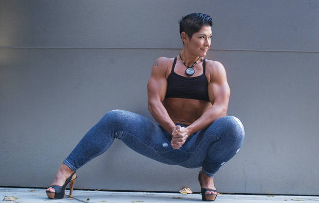 Kortney Olson Crouching down tensing her biceps and wearing jeans