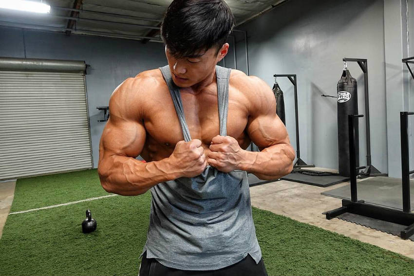 Long Wu tensing his biceps in a gym 