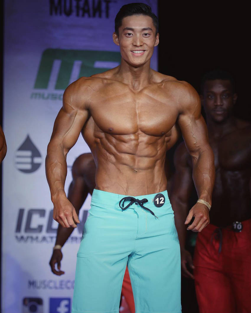 Long Wu standing in blue shorts at a physique competition