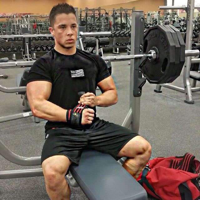 Nick Wright sitting on a bench in the gym securing his wrists with bodybuilding straps
