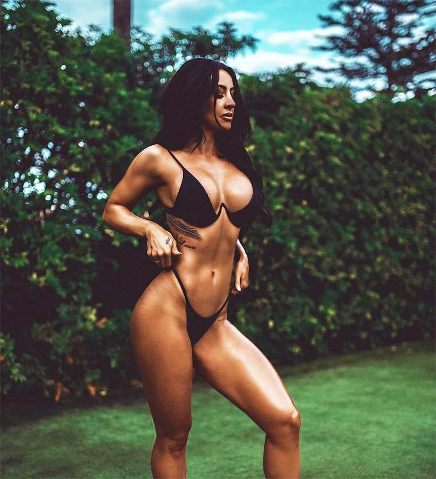 Steph Pacca posing in a black bikini in the garden, barefoot on the grass looking into the sunset. 