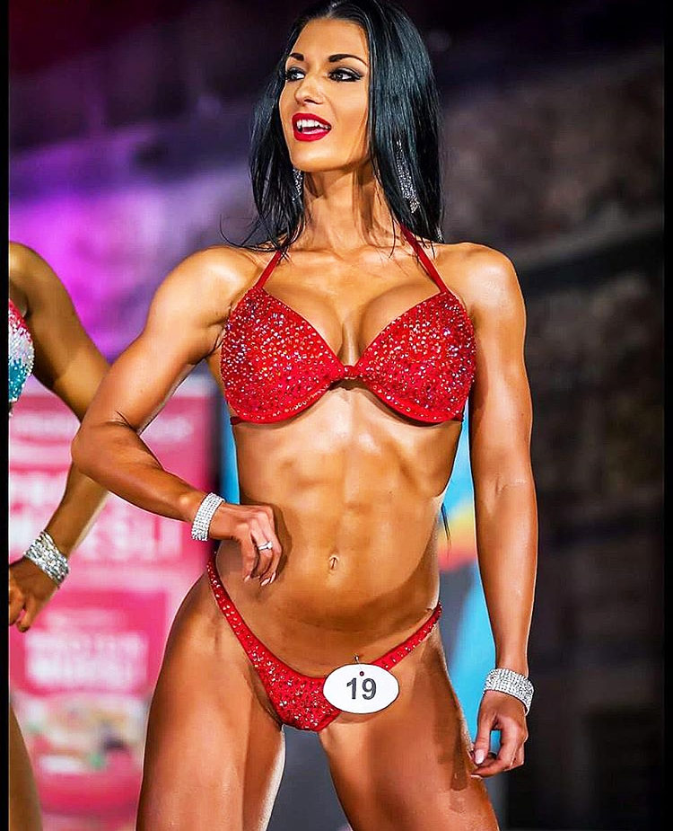 Valerija-Slapnik-posing-on-stage-as-a-bikini-athlete in a red bikini, showcasing her abs and muscular definition.