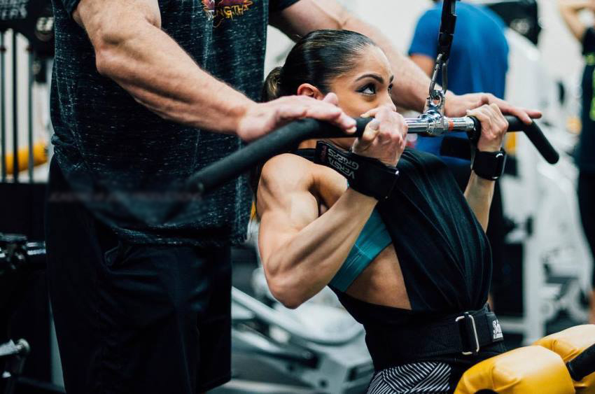 Ariel Khadr performing lat pulldowns with a man behind her who is spotting her