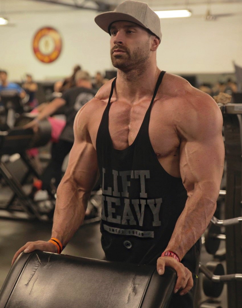 Bradley Martyn flexing his muscles while squeezing his hands against a bench