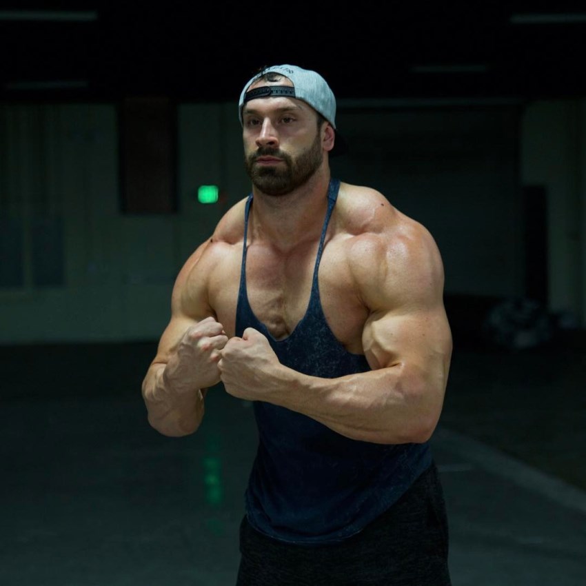 Bradley Martyn en camiseta de tirantes mostrando la pose más musculosa en el gimnasio