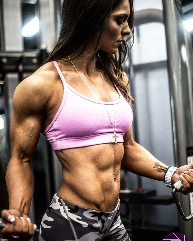 Christina Eleni performing a bicep curl in the gym looking strong and lean 