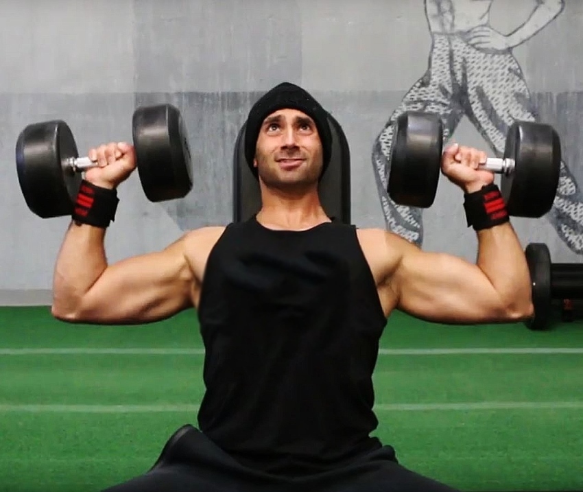 Dom Mazzetti doing a seated shoulder press on a bench