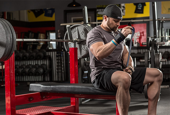 Layne Norton preparing to do a heavy bench press as he puts wrist wraps around his wrists