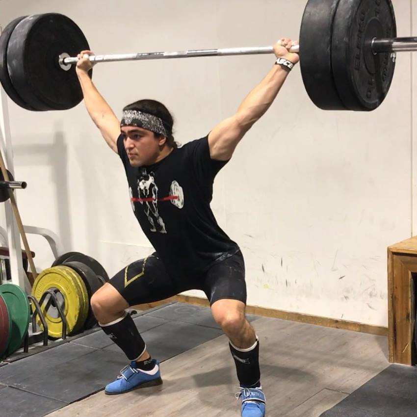 Omar Isuf doing an overhead press exercise with barbell