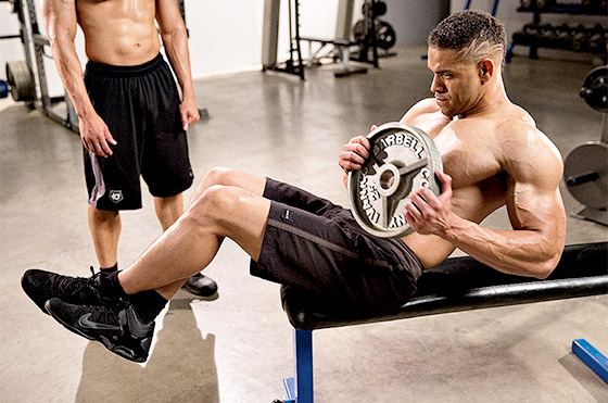 One of the Hodgetwins doing ab twists in a gym, while the other one is looking at him