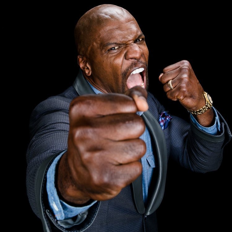 Terry Crews in a suit with an angry expression on his face pointing his fists and yelling at the camera