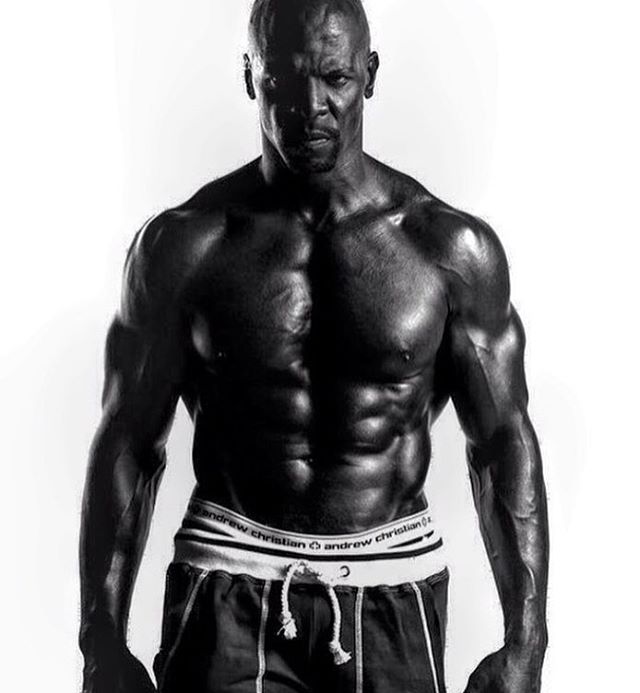 Terry Crews looking straight into the camera with a serious expression on his face, while having his shirt off, and showing his ripped upper body