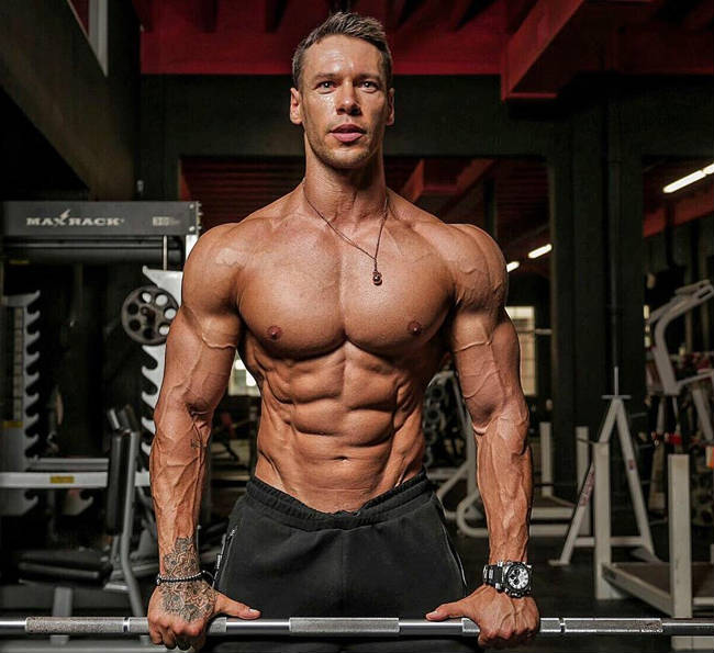 Anton Antipov holding onto a bar in the gym with his shirt off