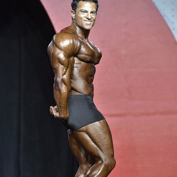 Arash Rahbar making waves on the Classic Olympia stage with his side triceps pose, displaying immaculate conditioning