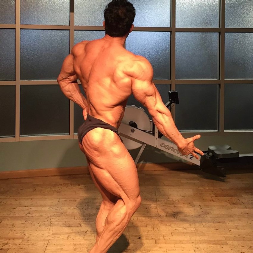 Arash Rahbar practicing posing in a room, his back and legs looking incredible from the side