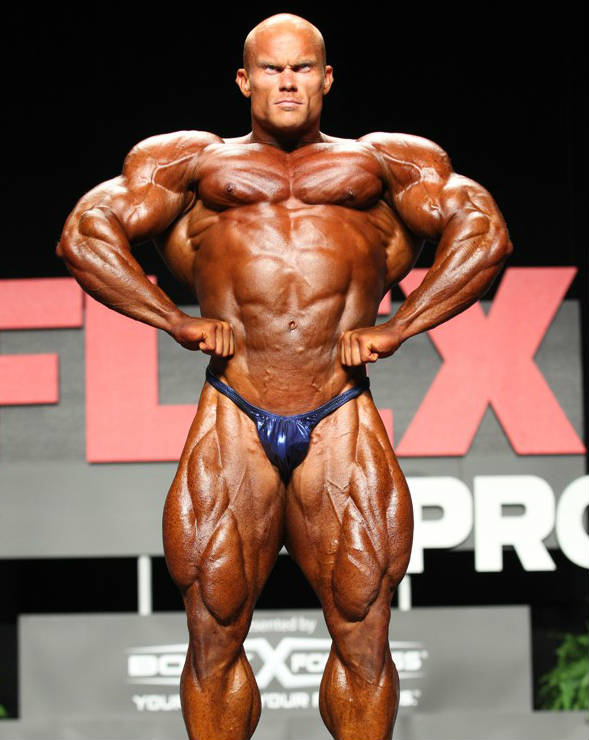 Ben Pakulski posing with his fists on his hips, showing his ripepd abs, large quadriceps and giant arms