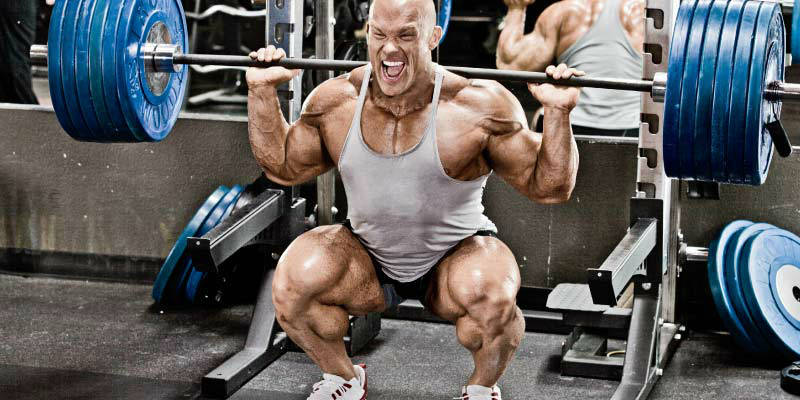Ben Pakulski completing a squat with a stacked barbell, showing his large quads arms and calves