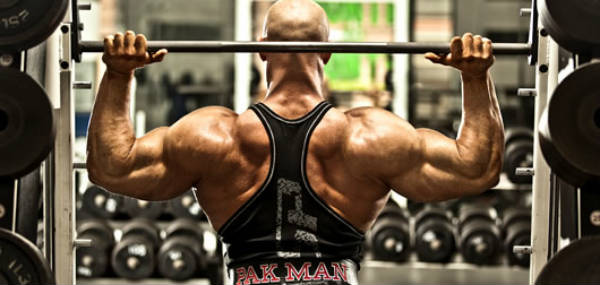 Ben Pakulski completing an overhead press with his large delts, back and 'pak man' weightlifting belt showing