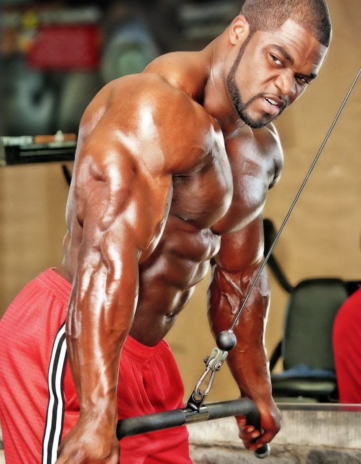 Brandon Curry doing cable triceps press, flexing his awesome arms, chest, and abs