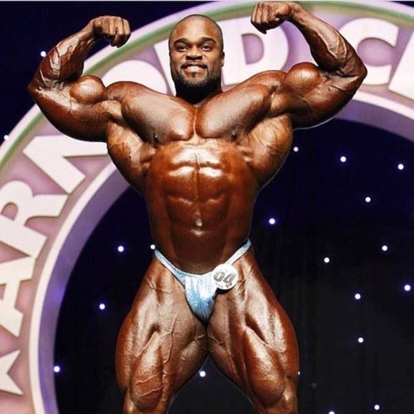 Brandon Curry performing a double biceps pose on the Arnold Classic stage