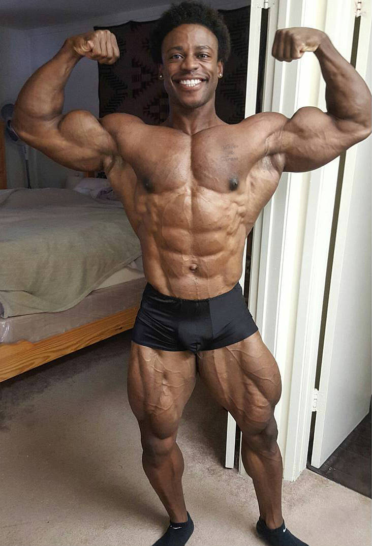 Breon Ansley standing and tensing his biceps, showing off his huge quads and arms
