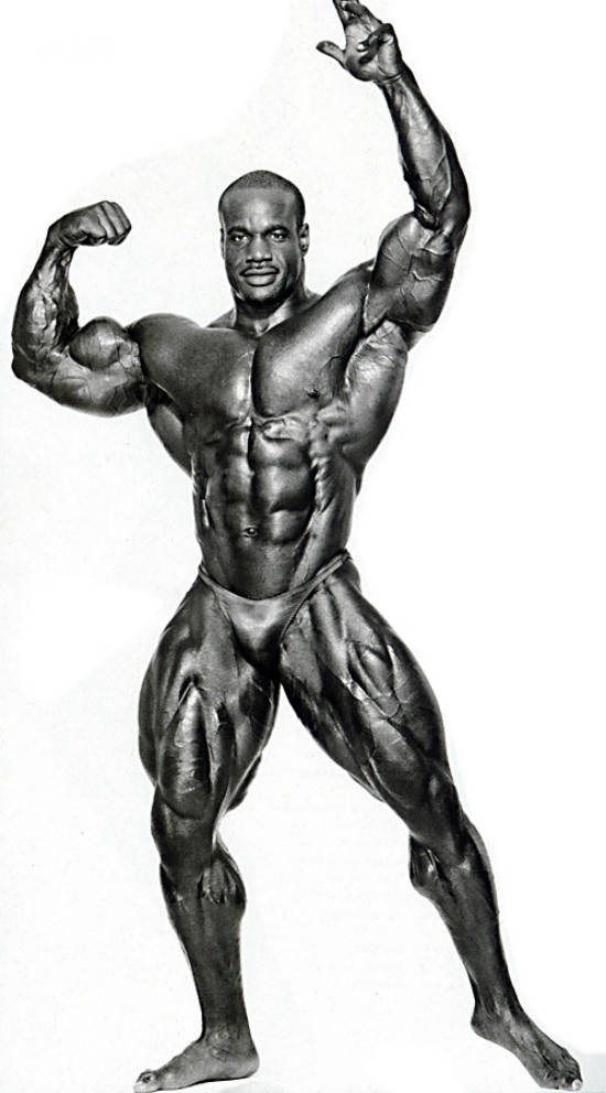 Chris Cormier posing, showing his massive quads, ripepd abs and large chest and arms 